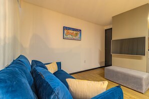 A living room with a blue sofa, a grey bench, a wall-mounted TV, and a map poster. - Homes Stay #2306 - Ideal Location in Carpediem (Recife)