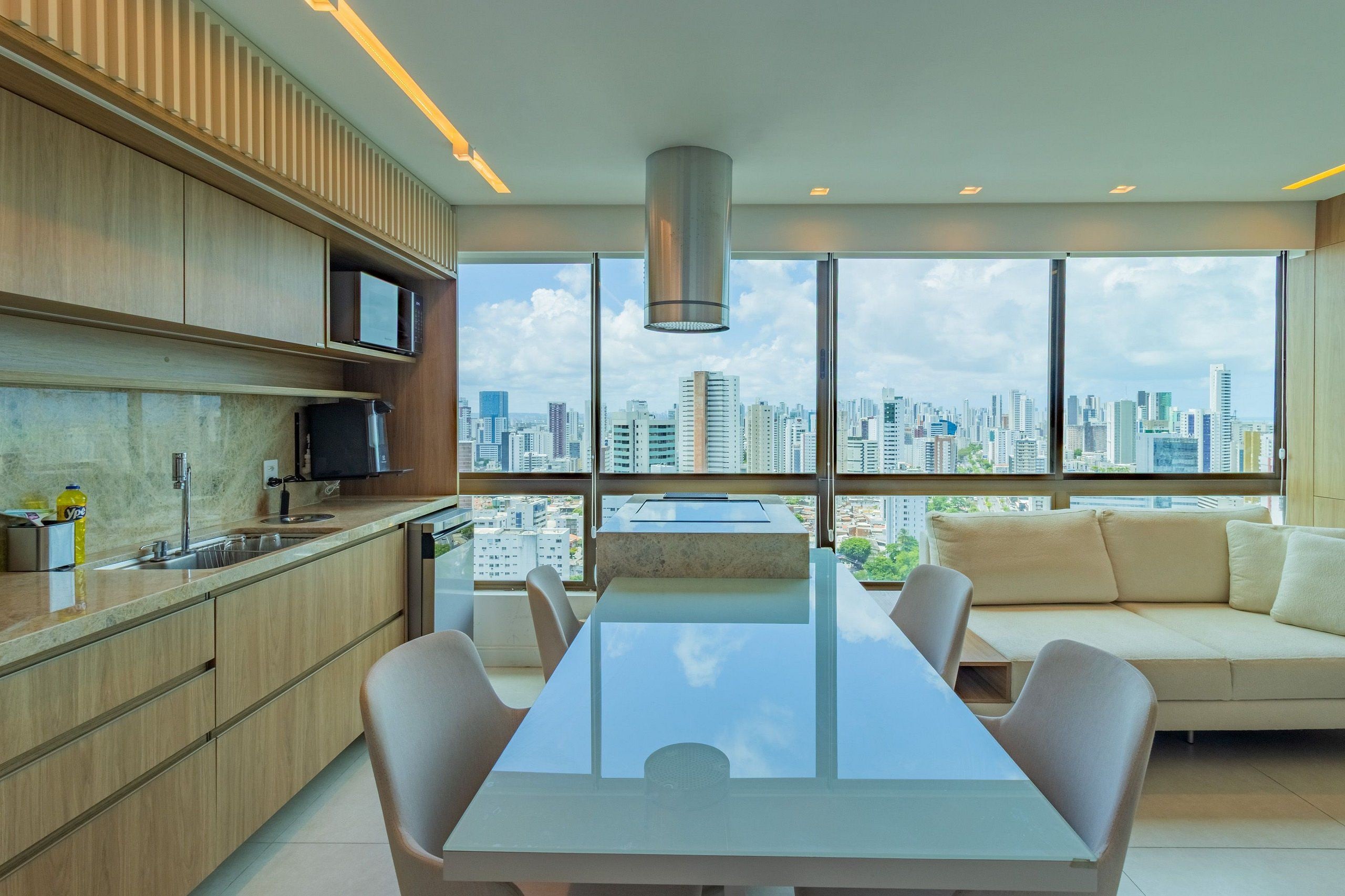 A modern kitchen with a large window overlooking a cityscape, a dining area with a glass table, and a sofa with a city view.