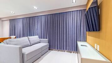 A modern hotel room with a grey sofa, a flat-screen TV mounted on the wall, and a wooden sideboard.