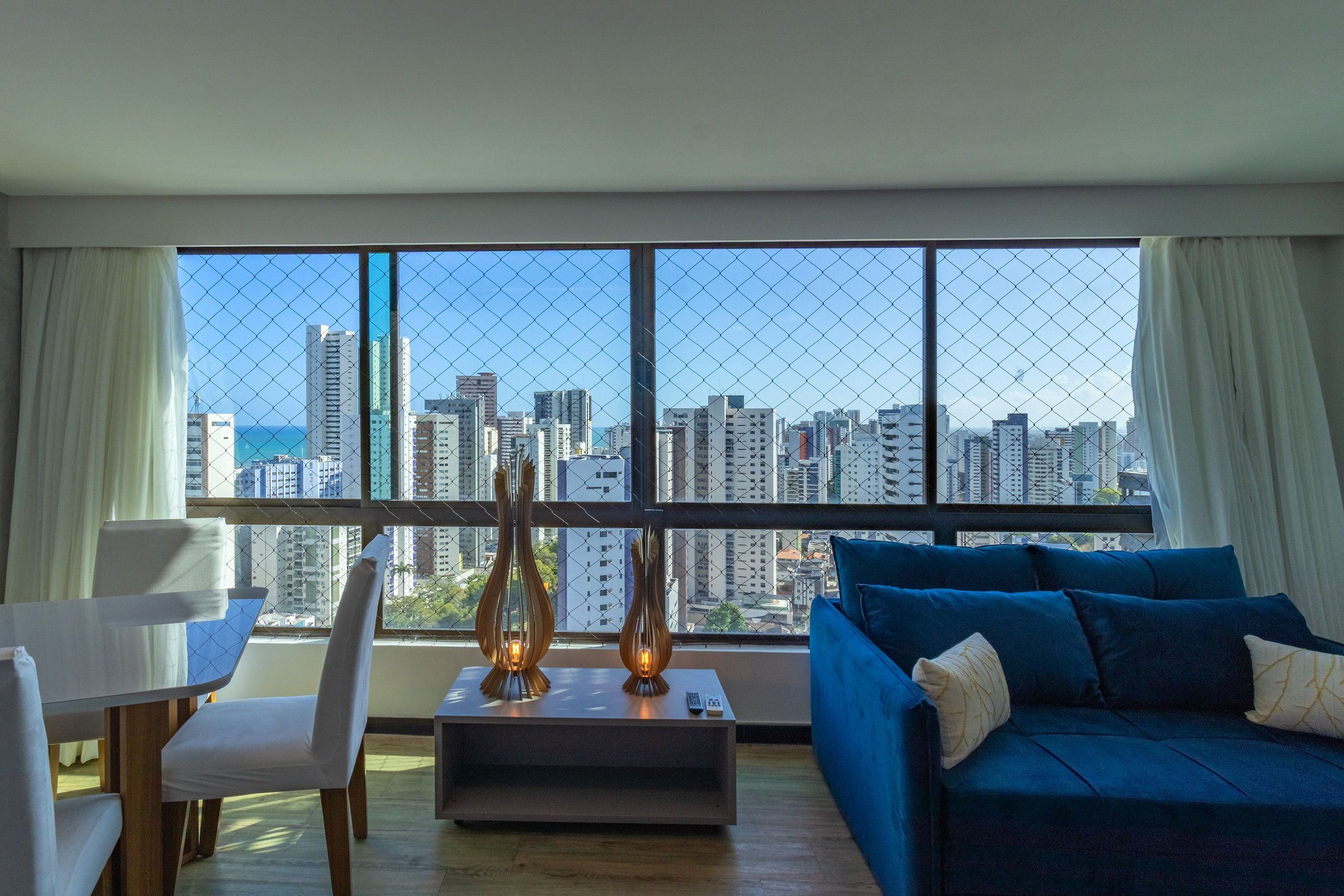 A modern living room with a large window, a blue sofa, a white chair, and a coffee table with two decorative vases.
