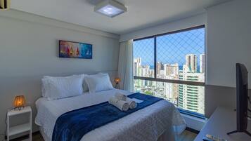 A hotel room with a large window, a bed with white bedding, a painting on the wall, and a desk with a remote control.