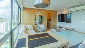 Una habitación de hotel moderna con un gran ventanal, zona de comedor, cocina y televisor.