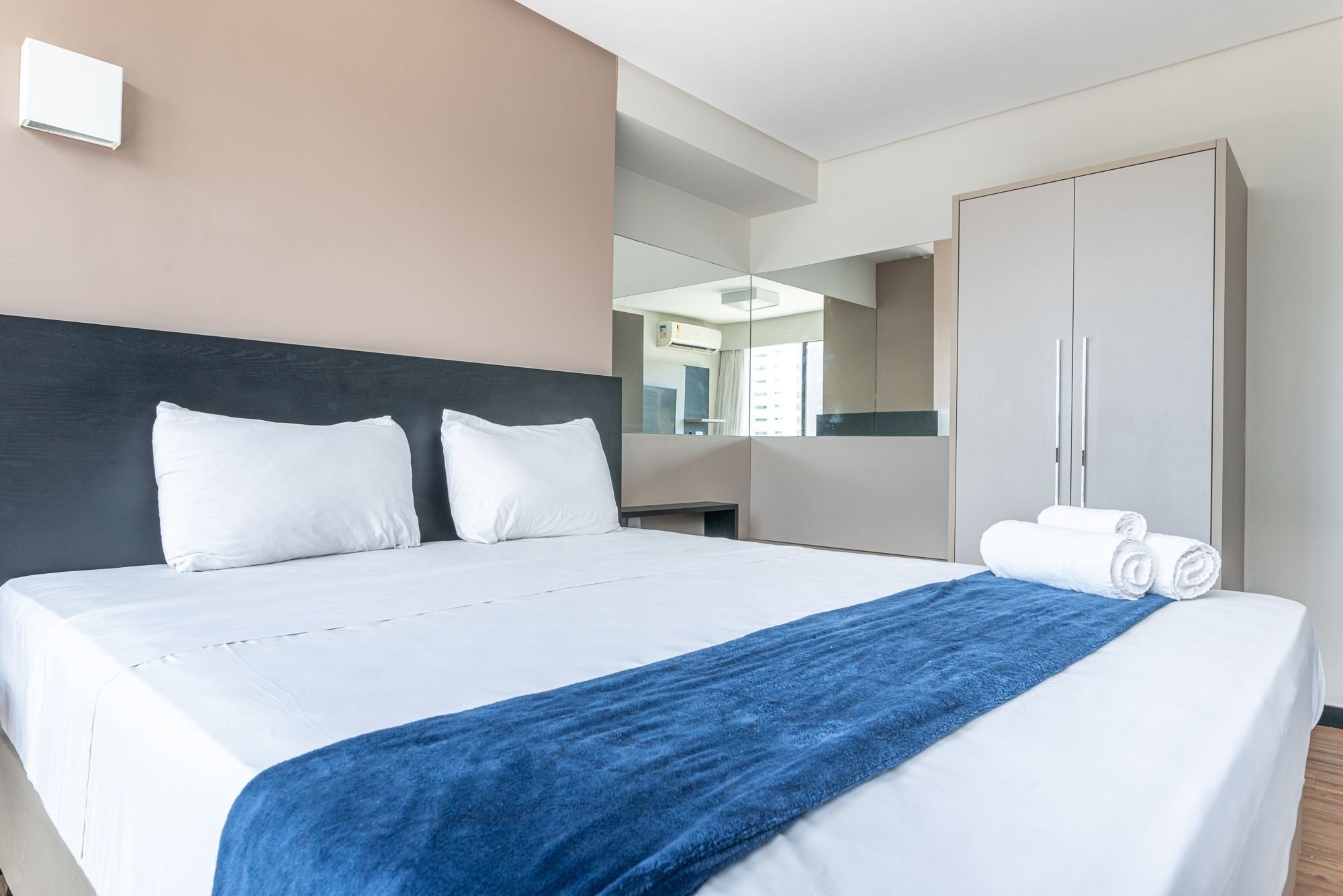 Une chambre d’hôtel avec un lit, une serviette bleue, une armoire et un miroir.