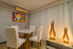 A dining area with a white table and chairs, an air conditioning unit, a colorful painting, and two decorative light fixtures. - Homes Stay #2306 - Ideal Location in Carpediem (Recife)
