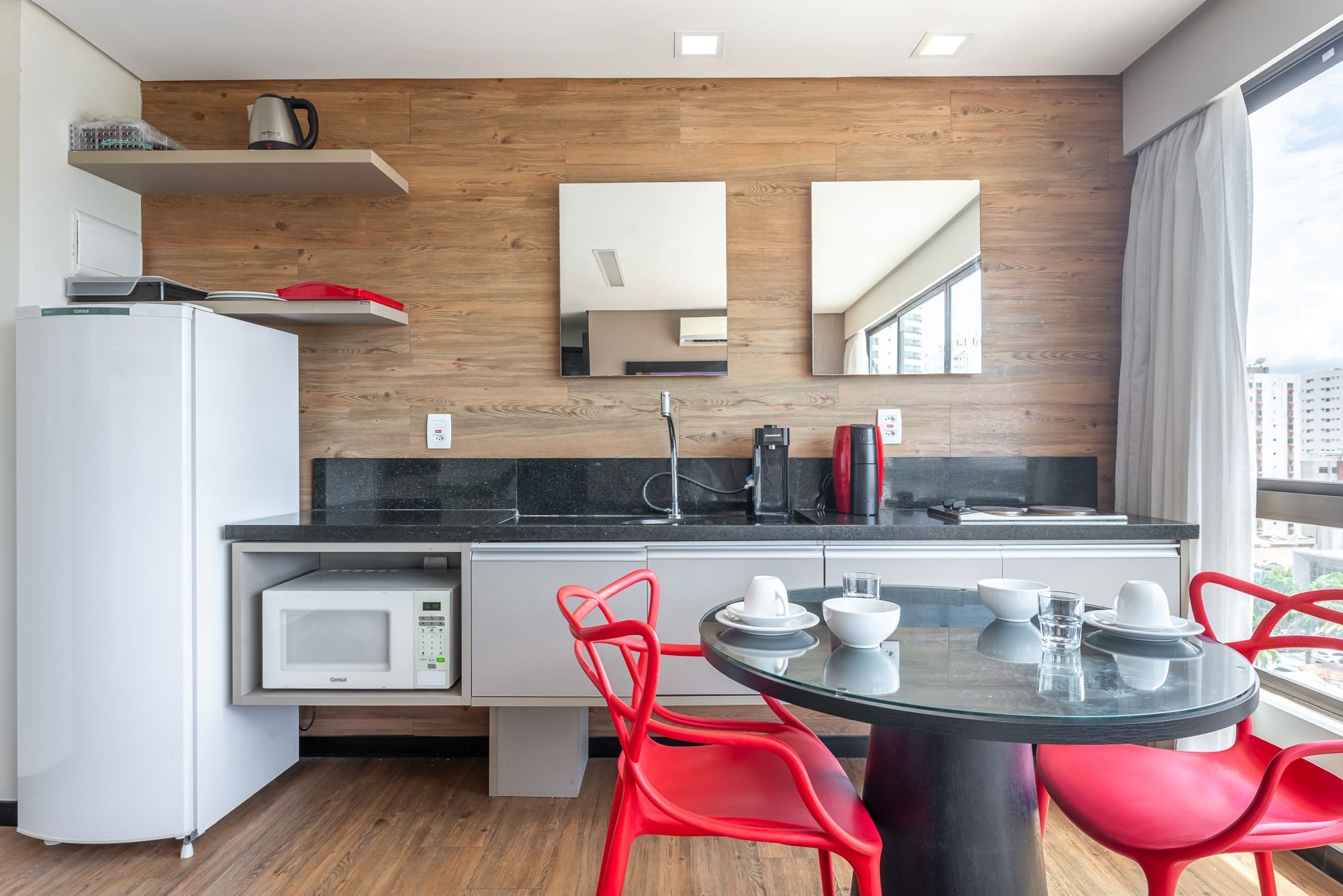 Une cuisine moderne équipée d’un four à micro-ondes, d’une machine à café et de chaises rouges.