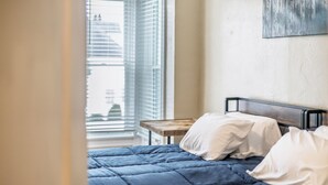 Ein Schlafzimmer mit einem Bett, Kissen, einem Nachttisch aus Holz und einem Fenster mit Jalousien.