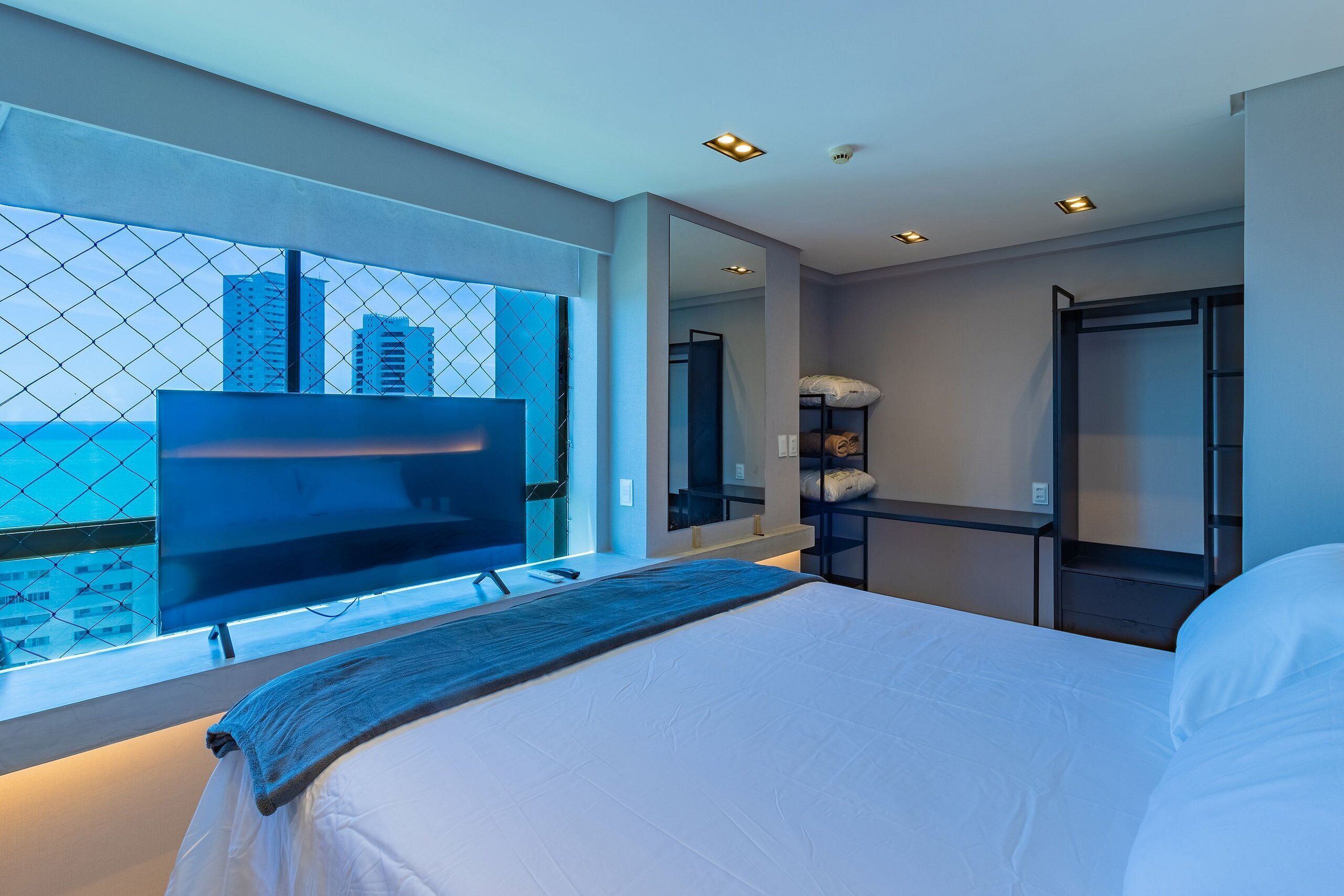 Habitación de hotel moderna con una cama grande, televisión, espejo y vista de la ciudad a través de una ventana.