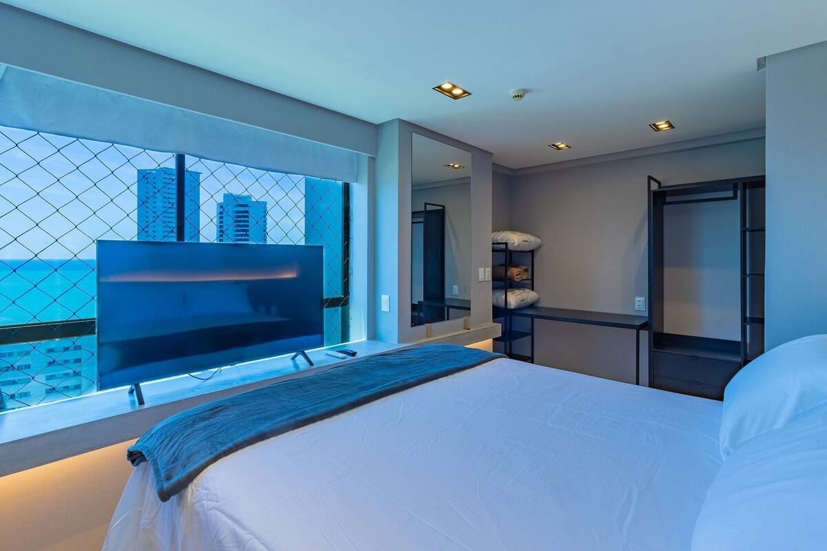Een moderne hotelkamer met een groot bed, een televisie, een spiegel en uitzicht op de stad door een raam.