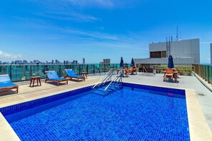 A rooftop pool with blue tiles, wooden lounge chairs, and a city skyline view. - Homes Stay #2307 - Flat em Recife by Carpediem (Recife)
