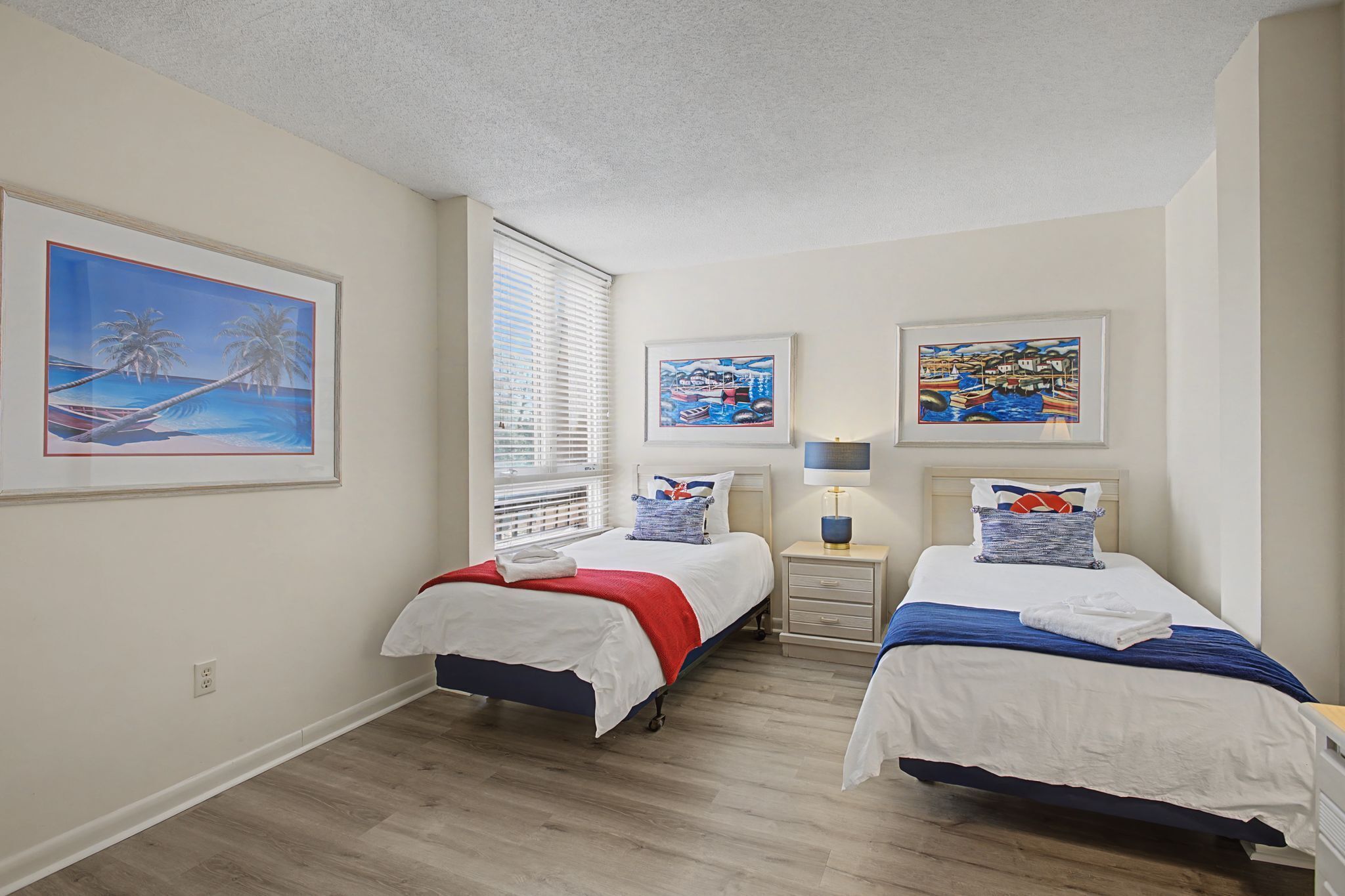 Une chambre d’hôtel avec deux lits, une fenêtre avec des stores et trois tableaux encadrés accrochés au mur.