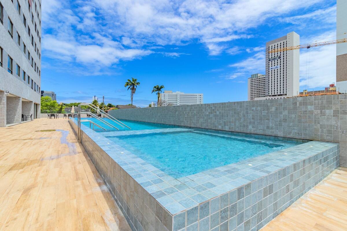 A rectangular pool with tiled edges, surrounded by a tiled wall and a wooden deck.