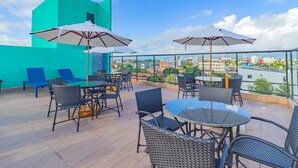 A rooftop terrace with outdoor seating, a glass balustrade, and a city view. - Varandas #415 - Porto de Galinhas por Carpediem (Ipojuca)