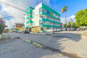 A multi-story building with a green and white facade, a paved street, and parked cars. - Varandas #415 - Porto de Galinhas por Carpediem (Ipojuca)
