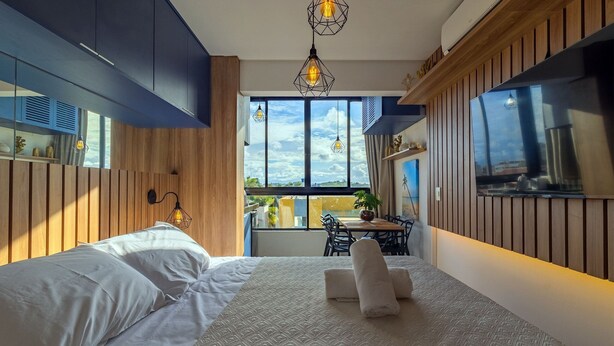 A hotel room with a bed, bedside table, lamp, and a window with a view. - Varandas #415 - Porto de Galinhas por Carpediem (Ipojuca)