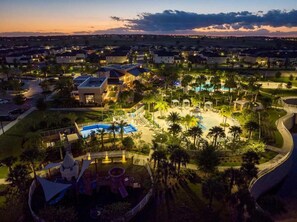 Ein Resort mit großem Pool, Palmen und einem gut beleuchteten Parkplatz.
