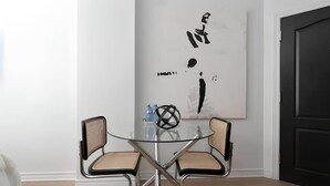 Ein moderner Essbereich mit einem Glastisch, zwei Stühlen, einem schwarzen abstrakten Gemälde an der Wand und einer dunklen Tür.