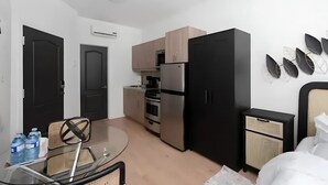 Eine kompakte Küche mit Kühlschrank, Backofen und Mikrowelle. Ein Esstisch mit Stühlen und ein kleines Schränkchen mit einer Mikrowelle sind vorhanden.