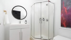 Ein modernes Badezimmer mit einem weißen Waschtisch, einer Duschkabine aus Glas und einer weißen Toilette.