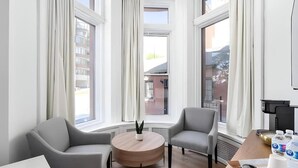 A modern room with two grey armchairs, a round wooden table, a potted plant, and a window with curtains.