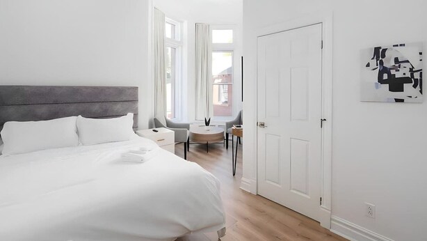 A modern hotel room with a large bed, a desk, and a chair. There is a door and a window in the room.