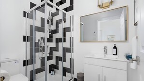 Une salle de bain moderne avec une douche à parois de verre, un lavabo blanc avec un miroir au-dessus et des toilettes.