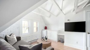 Een modern loft appartement met een schuine plafond, een grote televisie, een bank, een eethoek en een keuken.