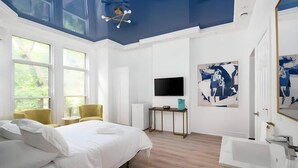 A modern bedroom with a large bed, a TV, a desk, and artwork on the wall.
