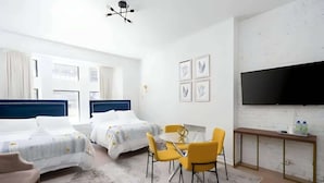 A hotel room with two beds, a dining table with chairs, a TV, and a small table with bottles. - Downtown Gem |2-Beds Condo • Prime location & Wifi (Montreal)