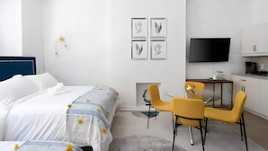 A modern bedroom with a bed, a desk, two chairs, a TV, and a fireplace. - Downtown Gem |2-Beds Condo • Prime location & Wifi (Montreal)