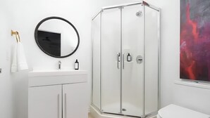 A modern bathroom with a white vanity, a glass shower enclosure, and a toilet. - Downtown Gem |2-Beds Condo • Prime location & Wifi (Montreal)