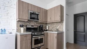 A compact kitchen with a built-in microwave, stove, and oven, wooden cabinets, and a marble backsplash. - Downtown Gem |2-Beds Condo • Prime location & Wifi (Montreal)
