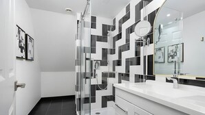 A modern bathroom with a glass-enclosed shower, a white vanity with a large mirror, and black and white patterned tiles on the walls. - The Suites | Downtown Montreal | 2 Beds (Montreal)