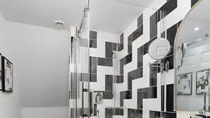 A modern bathroom with a shower, white cabinets, and a black and white tiled wall. - The Suites | Downtown Montreal | 2 Beds (Montreal)