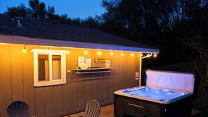 A hot tub with a wooden deck, two Adirondack chairs, and a small table with a fire pit. - Luxe Yosemite Retreat With Pool + Hot Tub + Game Room (Mariposa)