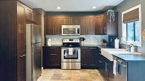 A modern kitchen with dark wooden cabinets, stainless steel appliances, and a tiled backsplash. - Luxe Yosemite Retreat With Pool + Hot Tub + Game Room (Mariposa)