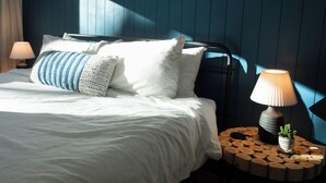 A neatly made bed with white and blue striped pillows, two bedside lamps, and a small plant on a wooden round table beside the bed. - Luxe Yosemite Retreat With Pool + Hot Tub + Game Room (Mariposa)
