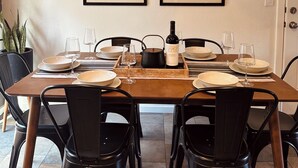 A dining area with a wooden table set for six, black chairs, a woven pendant light, and two framed botanical prints on the wall. - Luxe Yosemite Retreat With Pool + Hot Tub + Game Room (Mariposa)