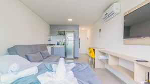Ein modernes Hotelzimmer mit einem Bett, einer Sitzecke, einer kleinen Küchenzeile und einem an der Wand befestigten Fernseher.