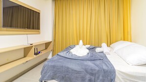 Ein Hotelzimmer mit Bett, Wandfernseher und einem Fenster mit gelben Vorhängen.