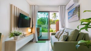 Een moderne woonkamer met een flatscreen televisie, een bank, een console tafel met een plant en uitzicht op een balkon met groen.