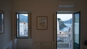 Una habitación con dos puertas abiertas que dan a un balcón con vistas a la costa.