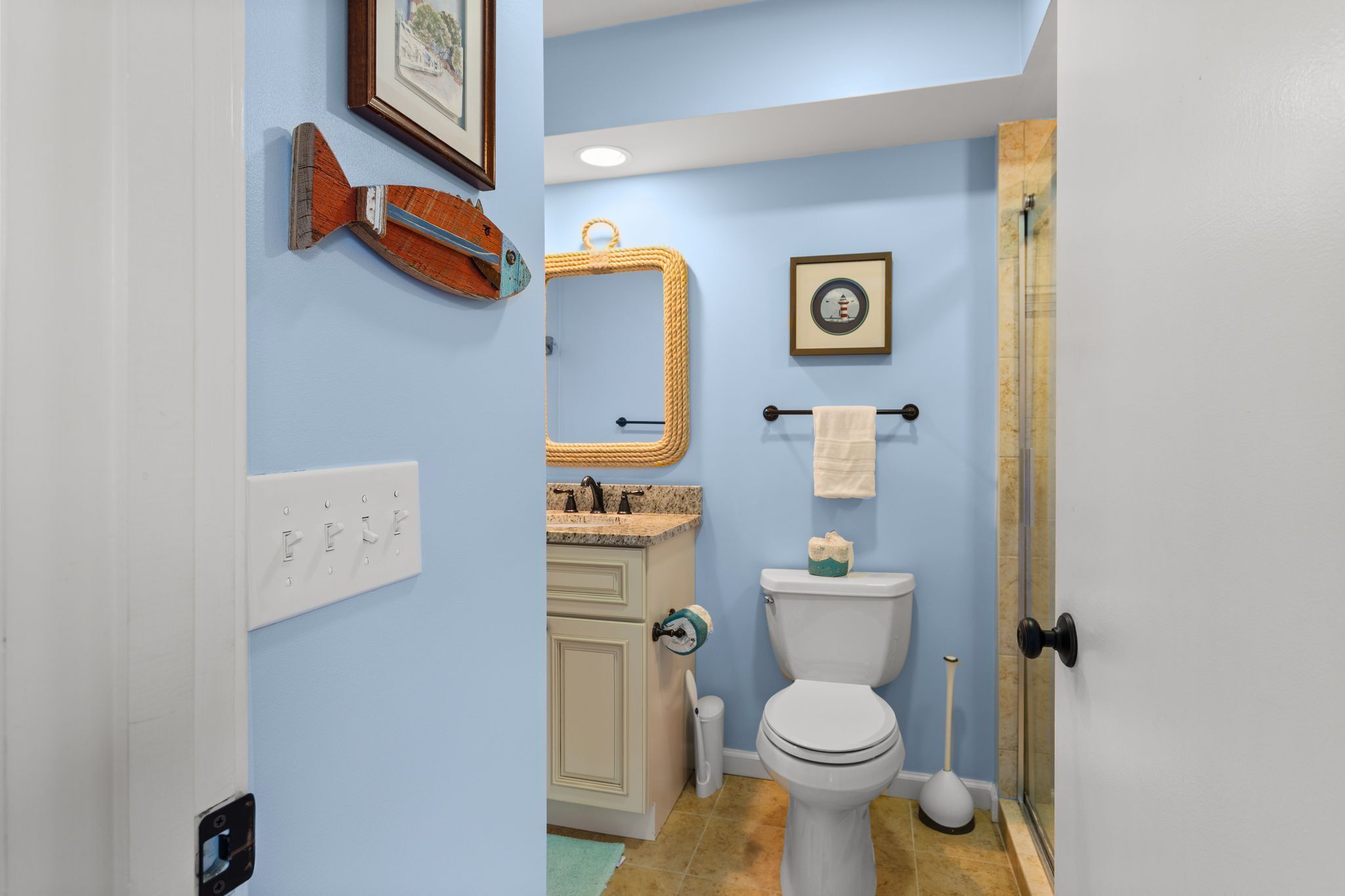 A bathroom with a white toilet, a sink with a marble countertop, a towel rack with a white towel, a framed mirror, and a framed picture on the wall.