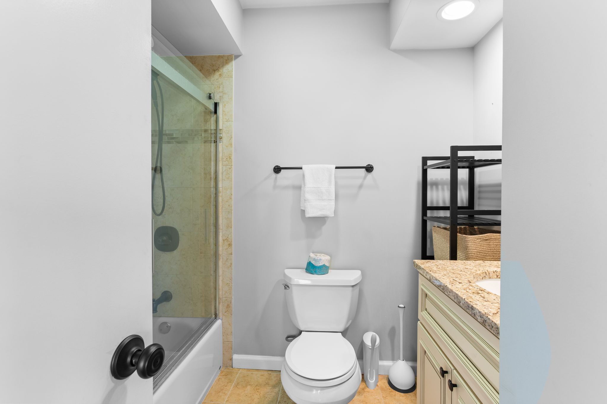 Un baño moderno con ducha de vidrio, inodoro con toallero y lavabo con encimera de granito.