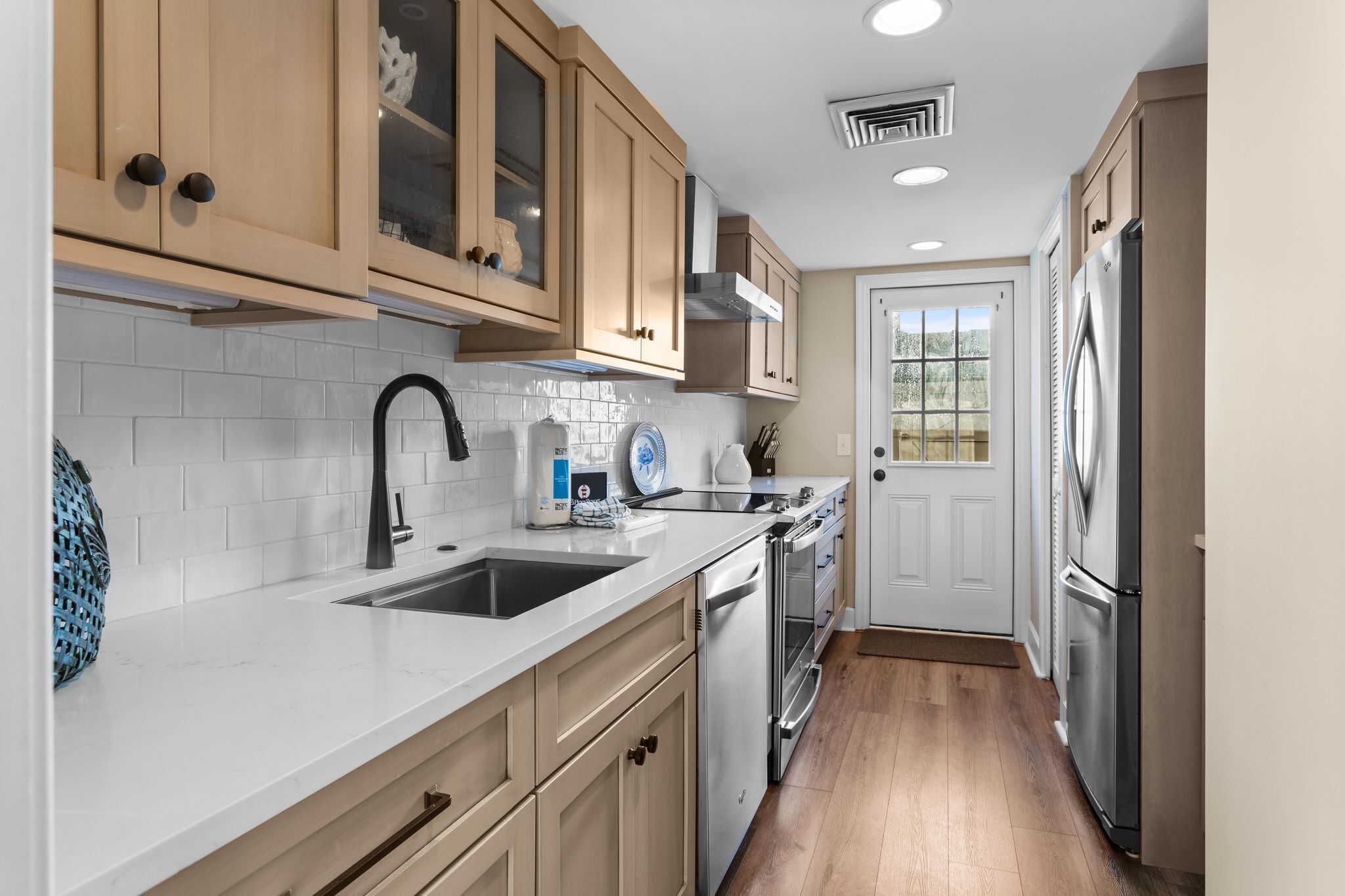 A kitchen with wooden cabinets, a stainless steel refrigerator, and a white tiled backsplash.