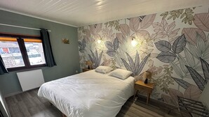 A bedroom with a bed, a nightstand, a lamp, a window with curtains, and a wall with a leaf pattern. - Charming family gîte "Le Nid de Chartreuse" in Saint Christophe la Grotte (Saint-Christophe)