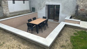 A patio area with a wooden table and chairs, a concrete border, and a stone wall. - Charming family gîte "Le Nid de Chartreuse" in Saint Christophe la Grotte (Saint-Christophe)