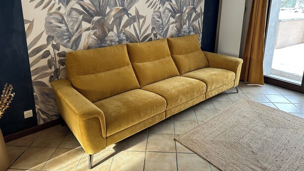 A mustard-colored sofa against a wall with a tropical leaf pattern, a tiled floor, and a view through a window with curtains. - Charming family gîte "Le Nid de Chartreuse" in Saint Christophe la Grotte (Saint-Christophe)