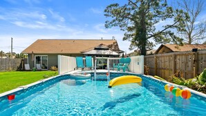 Ein Garten mit Swimmingpool, einer Holzterrasse und einem eingezäunten Bereich.