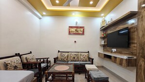 A living room with a sofa, chairs, a coffee table, a TV mounted on a wooden shelf, and a ceiling fan. - Casa InteliStay – Smart, Stylish 2BHK in Lucknow (Lucknow)