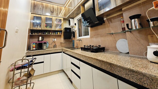 A kitchen with wooden cabinets, a granite countertop, a built-in microwave, a coffee maker, and a kettle. - Casa InteliStay – Smart, Stylish 2BHK in Lucknow (Lucknow)